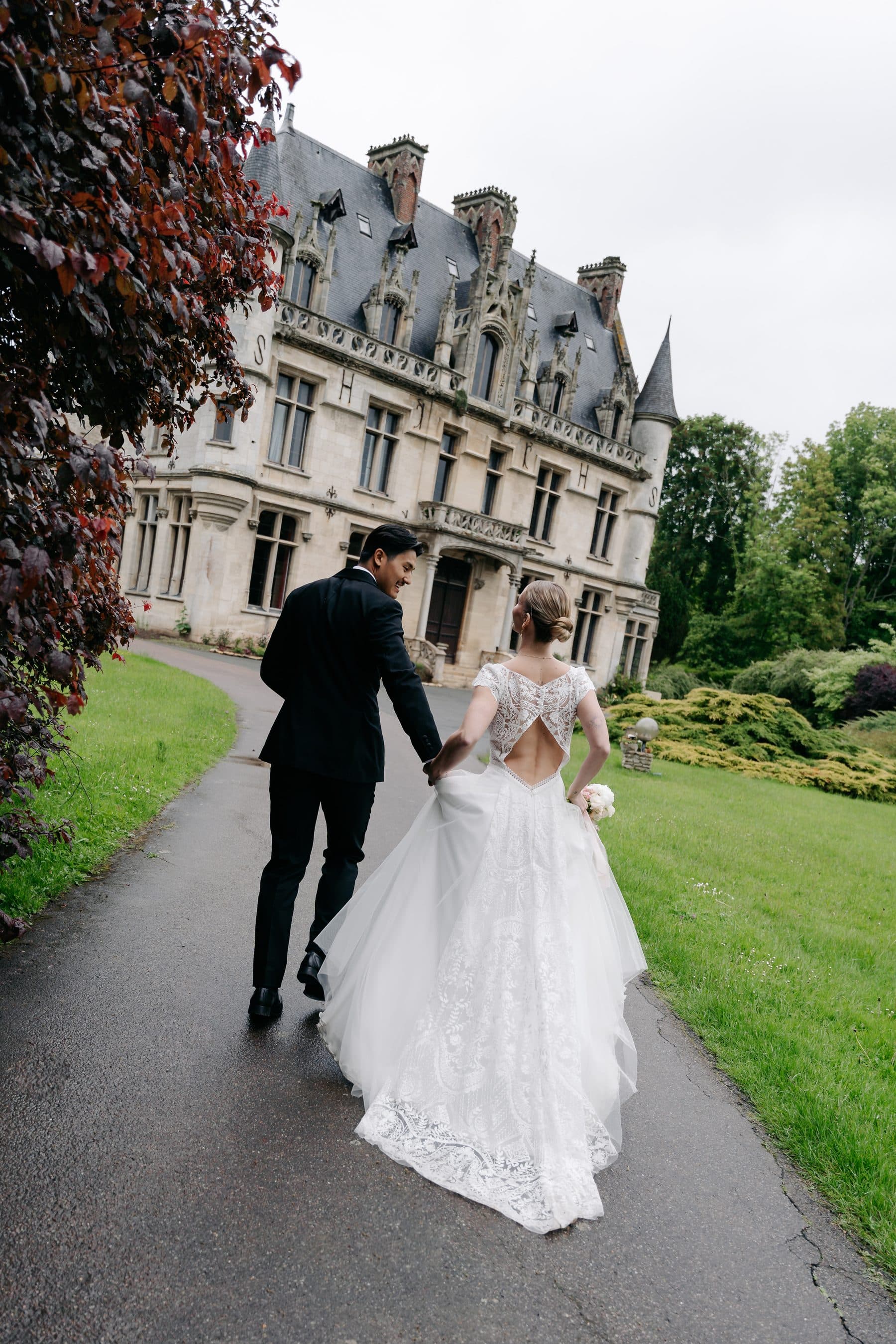 Les mariés marchant dans l'allée du parc, devant le château
