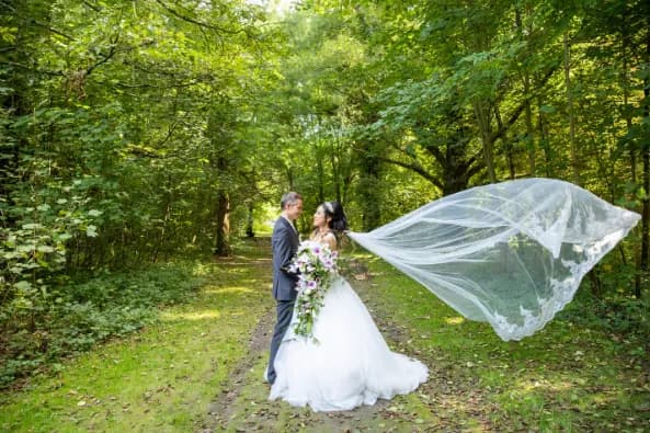 Photographie de mariage signée Georges Vuong, le voile déployé sur un chemin en sous-bois